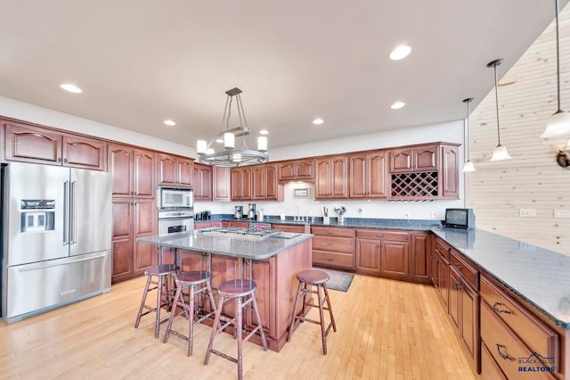 kitchen with pendant lighting, wood walls, light hardwood / wood-style floors, a kitchen bar, and stainless steel appliances