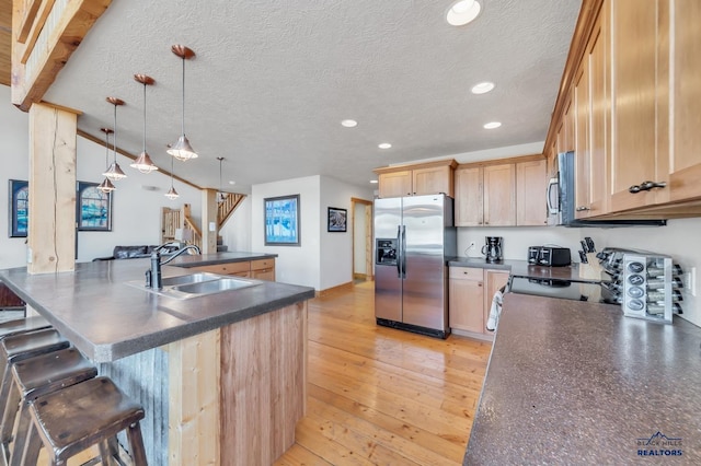 kitchen with stainless steel appliances, sink, light brown cabinets, light hardwood / wood-style floors, and hanging light fixtures