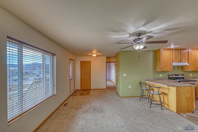 kitchen featuring kitchen peninsula, a kitchen breakfast bar, light colored carpet, ceiling fan, and electric stove