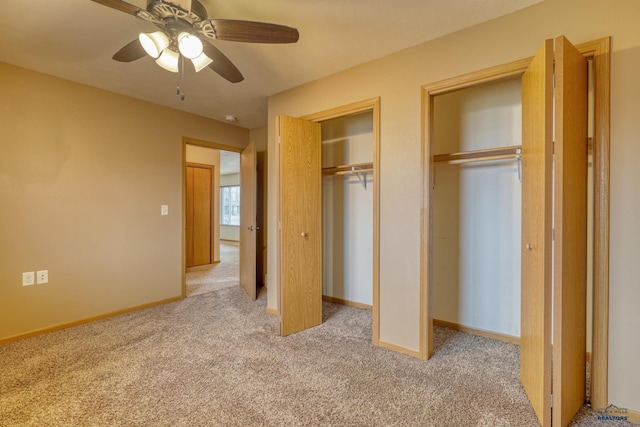 unfurnished bedroom with ceiling fan, light colored carpet, and two closets