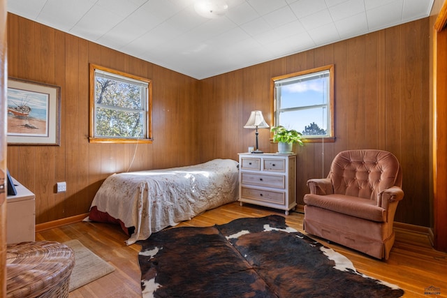 bedroom with wood walls, light hardwood / wood-style floors, and multiple windows