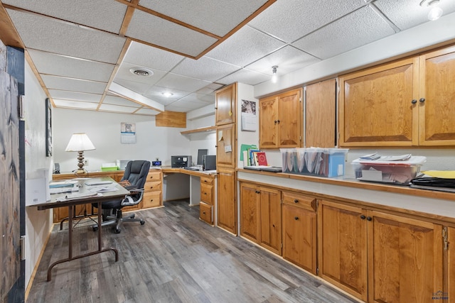 office space with a drop ceiling, built in desk, and light hardwood / wood-style flooring