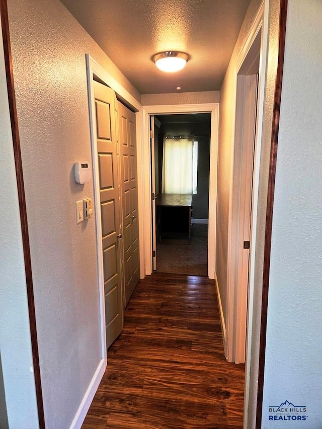 corridor with dark hardwood / wood-style flooring and a textured ceiling