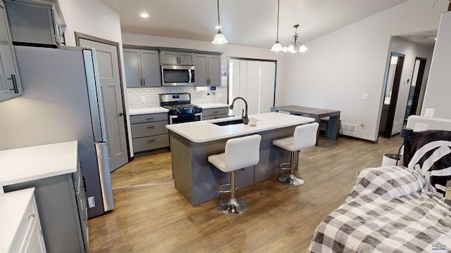 kitchen with appliances with stainless steel finishes, gray cabinetry, sink, a center island with sink, and light hardwood / wood-style flooring