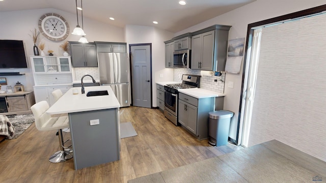 kitchen featuring stainless steel appliances, pendant lighting, lofted ceiling, light hardwood / wood-style floors, and a breakfast bar