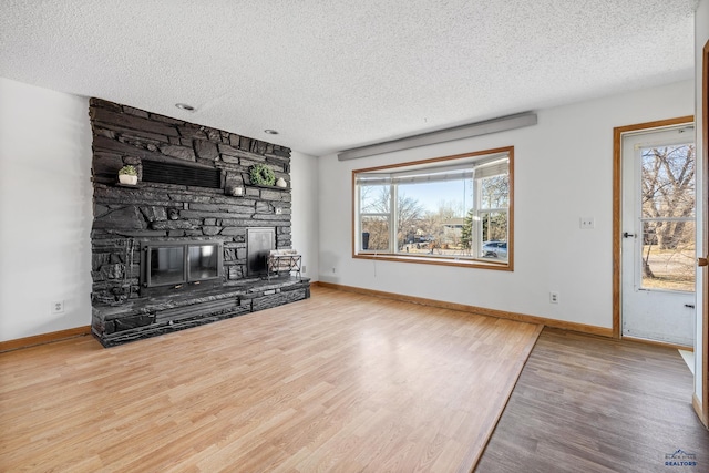 unfurnished living room featuring hardwood / wood-style floors, a stone fireplace, and a textured ceiling