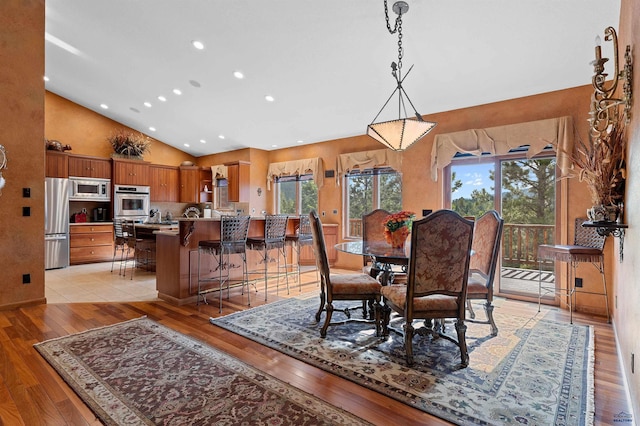 dining space with high vaulted ceiling and light hardwood / wood-style flooring