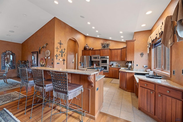 kitchen featuring light stone counters, stainless steel appliances, a kitchen island with sink, light hardwood / wood-style floors, and a breakfast bar area