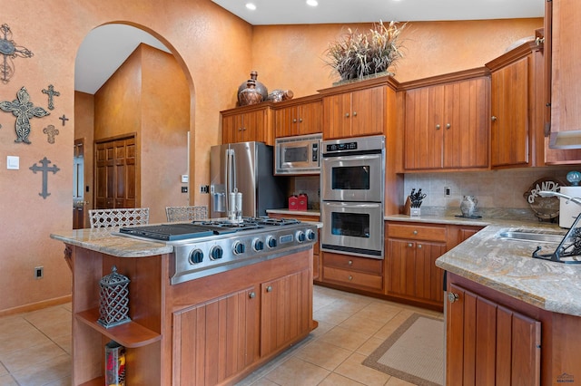 kitchen featuring sink, decorative backsplash, light tile patterned floors, appliances with stainless steel finishes, and a kitchen island