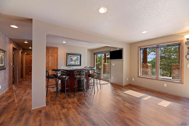 dining space featuring bar area, dark wood-type flooring, and a textured ceiling