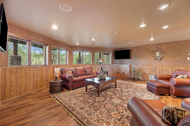 living room with hardwood / wood-style floors, wood walls, and a textured ceiling