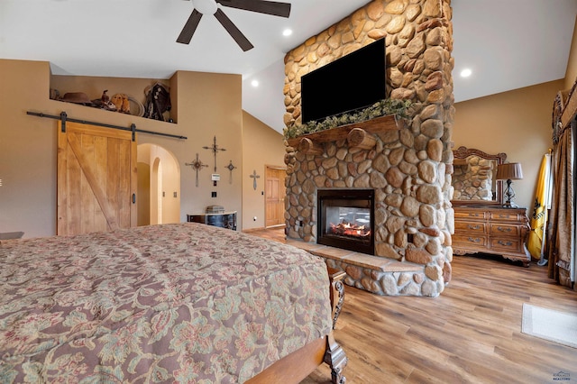 bedroom featuring ceiling fan, a barn door, a stone fireplace, high vaulted ceiling, and wood-type flooring