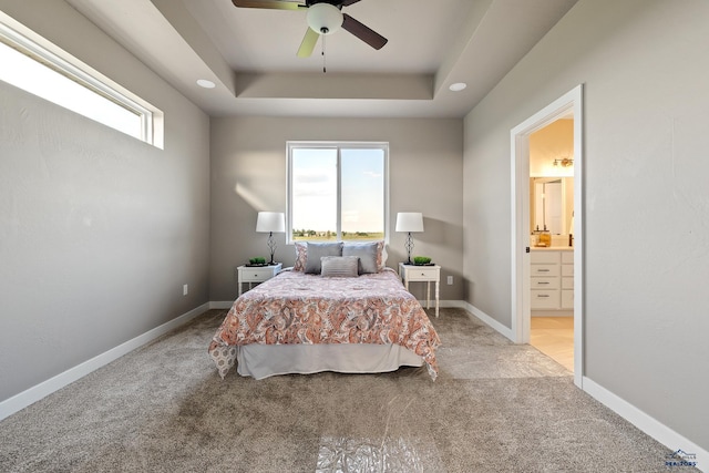 carpeted bedroom with ensuite bathroom, a raised ceiling, multiple windows, and ceiling fan