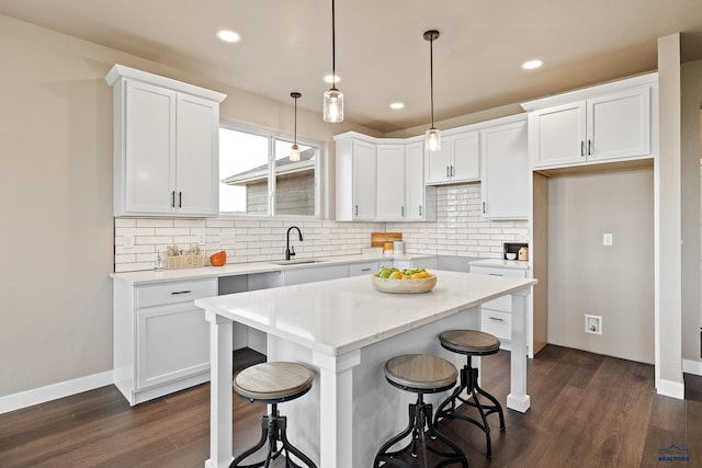 kitchen with dark wood-type flooring, sink, white cabinets, a kitchen island, and hanging light fixtures