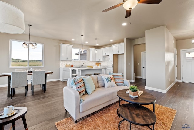 living room with ceiling fan with notable chandelier, wood-type flooring, and sink