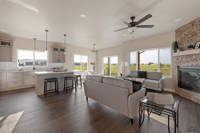 living room featuring dark hardwood / wood-style floors, a stone fireplace, and ceiling fan