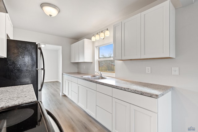 kitchen with black fridge, sink, white cabinets, and light hardwood / wood-style floors