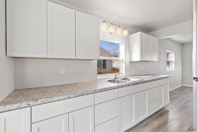 kitchen with white cabinets, light stone countertops, sink, and light hardwood / wood-style flooring