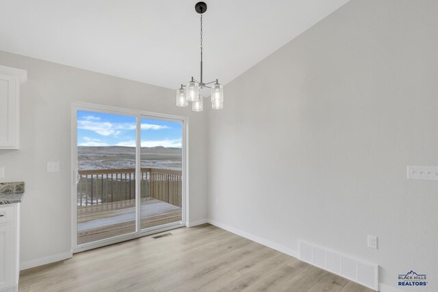 unfurnished dining area featuring a chandelier, light wood-type flooring, and lofted ceiling