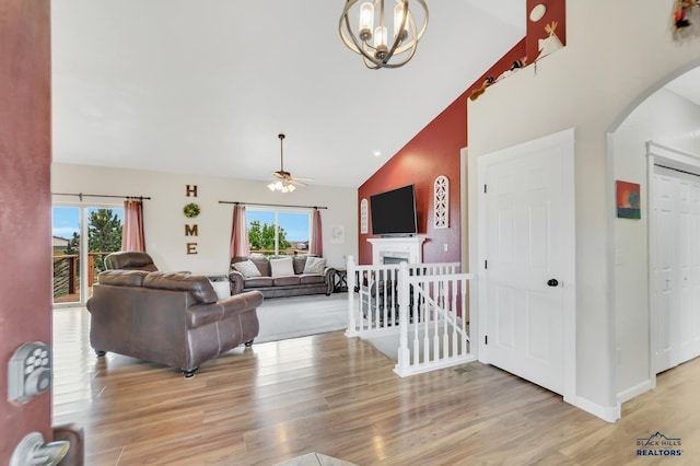 living room featuring ceiling fan with notable chandelier, a healthy amount of sunlight, light wood-type flooring, and high vaulted ceiling