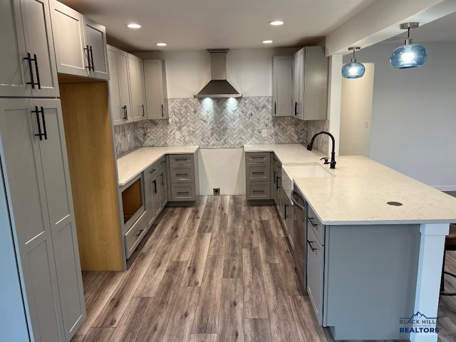 kitchen featuring wall chimney exhaust hood, dark hardwood / wood-style floors, kitchen peninsula, decorative light fixtures, and gray cabinets