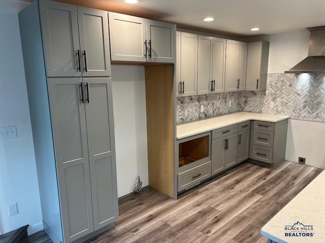 6920 Long View Rd, Rapid City, SD 57703 - kitchen with wall chimney exhaust hood, gray cabinetry, recessed lighting, wood finished floors, and decorative backsplash