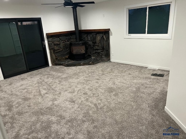 living room featuring a wood stove, ceiling fan, and carpet floors