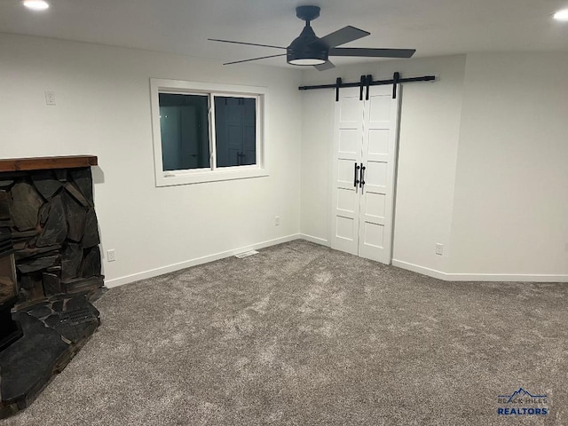 unfurnished living room featuring a barn door, ceiling fan, and carpet floors