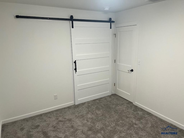 unfurnished bedroom featuring a barn door and dark colored carpet