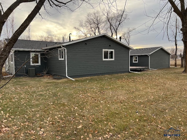 back house at dusk with a yard and central AC