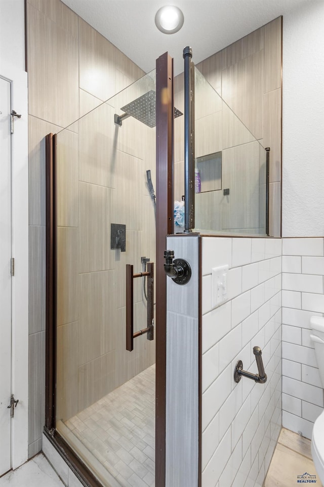 bathroom with a shower with door, toilet, and tile walls