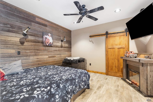 bedroom featuring a barn door, ceiling fan, and light hardwood / wood-style floors