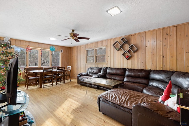 living room with a textured ceiling, light wood-type flooring, ceiling fan, and wooden walls