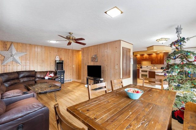 dining area with ceiling fan, light hardwood / wood-style floors, a textured ceiling, and wooden walls