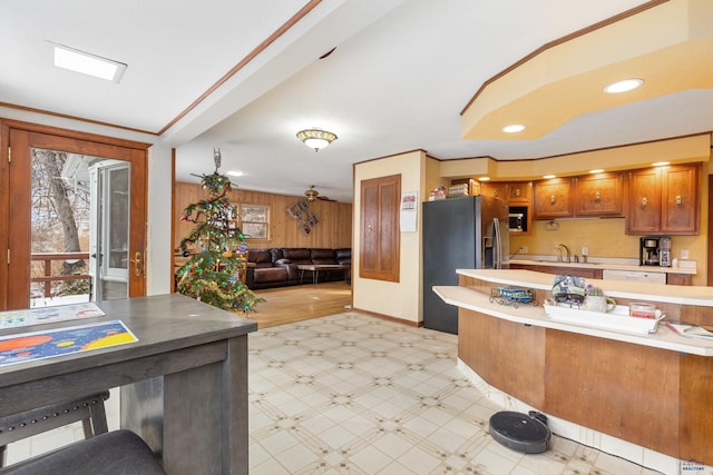 kitchen featuring kitchen peninsula, wooden walls, sink, fridge with ice dispenser, and a breakfast bar area