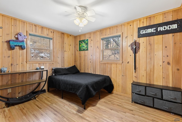 bedroom with light hardwood / wood-style flooring, ceiling fan, and wood walls