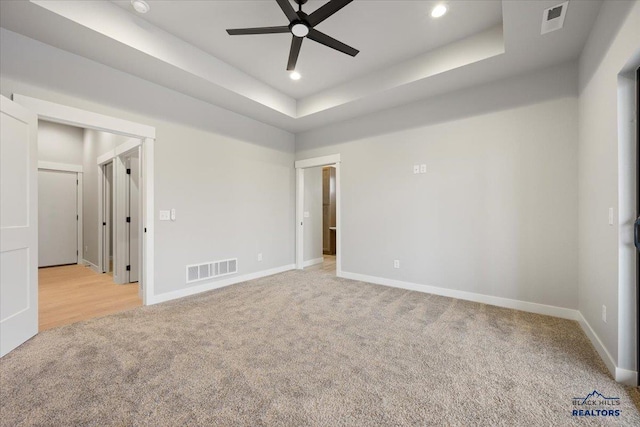 carpeted spare room with a raised ceiling and ceiling fan