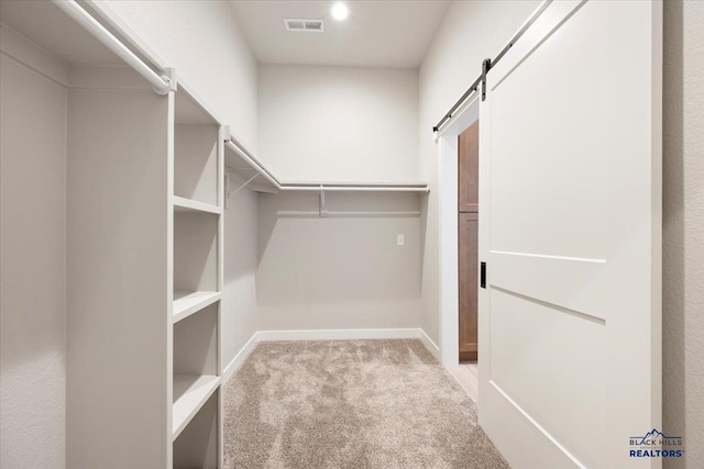 walk in closet with light carpet and a barn door