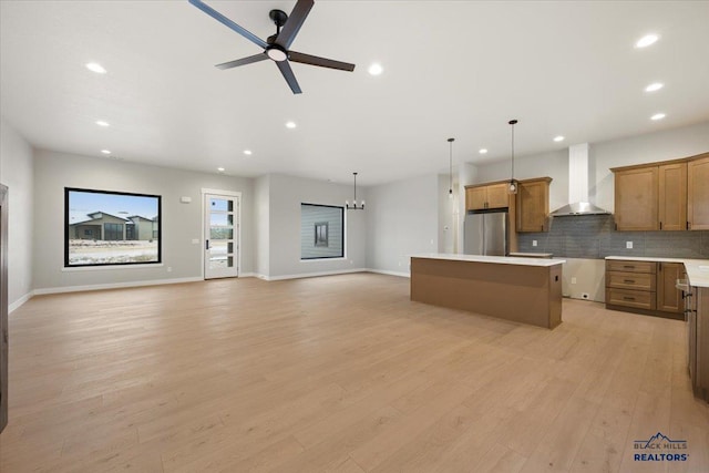 kitchen featuring stainless steel refrigerator, hanging light fixtures, wall chimney range hood, light hardwood / wood-style flooring, and a kitchen island