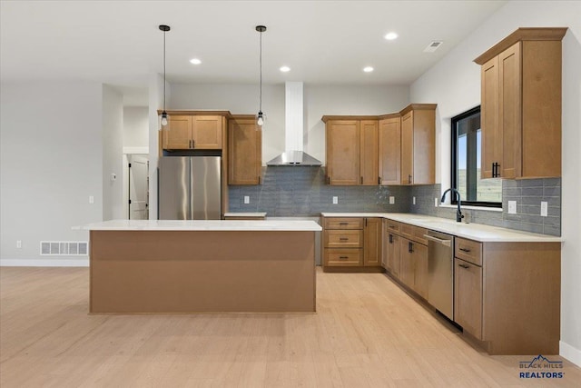 kitchen featuring a center island, sink, stainless steel appliances, wall chimney range hood, and light wood-type flooring