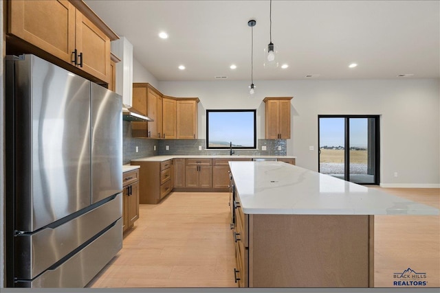 kitchen featuring stainless steel refrigerator, light stone countertops, a center island, hanging light fixtures, and light wood-type flooring