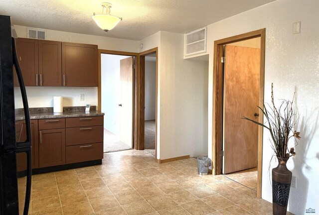 kitchen with dark stone countertops, black fridge, and a textured ceiling