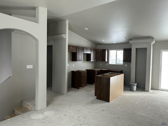 kitchen with a center island, vaulted ceiling, a textured ceiling, and dark brown cabinetry