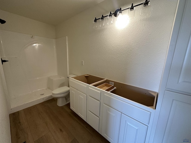 bathroom with a shower, toilet, a textured wall, and wood finished floors