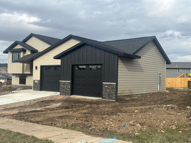 view of front of home with driveway, stone siding, board and batten siding, a shingled roof, and a garage