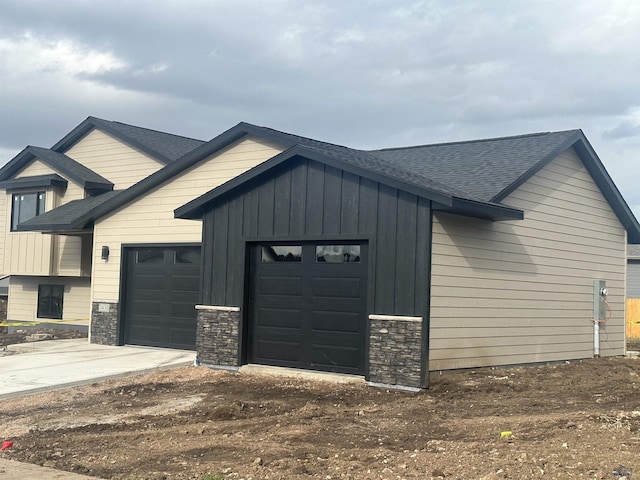 view of front of property featuring stone siding, a garage, concrete driveway, board and batten siding, and a shingled roof