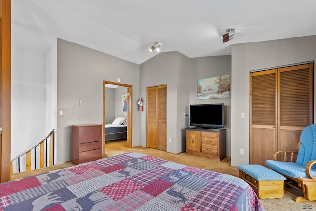 bedroom with vaulted ceiling, light colored carpet, and multiple closets