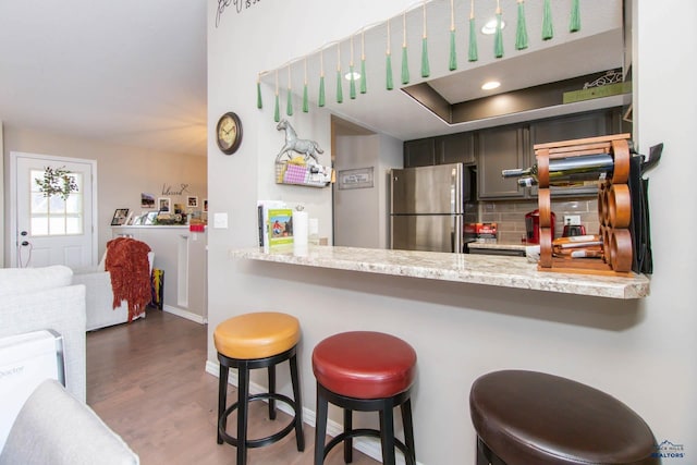 kitchen with light stone countertops, tasteful backsplash, dark hardwood / wood-style floors, stainless steel fridge, and a breakfast bar area