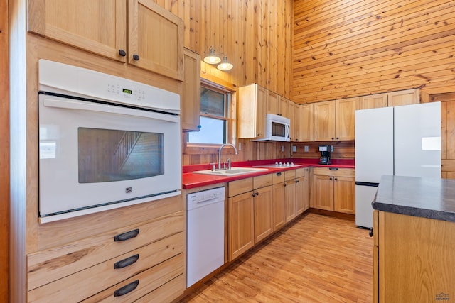 kitchen with sink, light brown cabinetry, white appliances, and wood walls