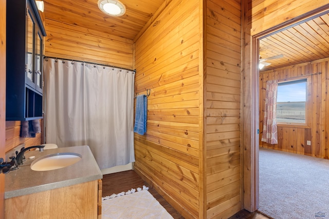 bathroom with ceiling fan, wood walls, wood ceiling, and vanity